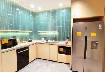 Communal kitchen area featuring teal tiled walls, light wood cabinetry, and a large stainless steel refrigerator.
