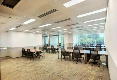 Large open-plan office with multiple rows of wooden desks and black ergonomic chairs.