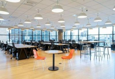 Bright open-plan workspace with rows of desks, ergonomic chairs, and many pendant lights.