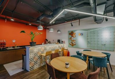 Communal kitchen area featuring a patterned tile backsplash, orange accent wall, and wooden cafe tables.