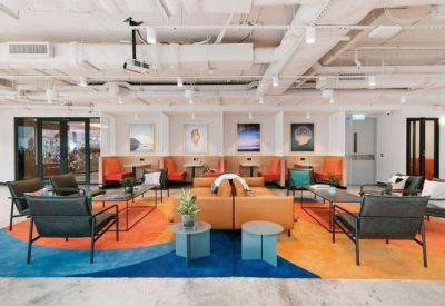 Spacious communal lounge with diverse seating, a colorful patterned rug, and industrial ceilings.