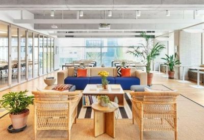 Vibrant reception lounge with wicker armchairs, a blue sofa, and glass-walled meeting rooms.