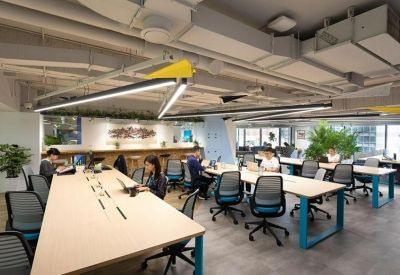 Open-plan office space with rows of light wood desks and ergonomic blue chairs.