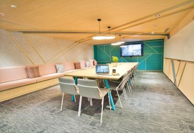 Long conference table in a meeting room with soft lighting and a wall-mounted screen.