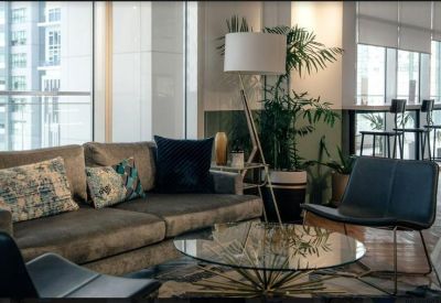 Bright lounge area with a grey sofa, glass coffee table, and indoor plants.