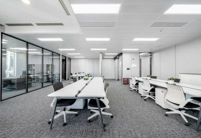 Large open-plan workspace with multiple rows of white desks and ergonomic chairs under bright panel lighting.