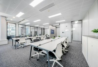 Professional coworking area with shared white desks and glass-walled private offices in the background.