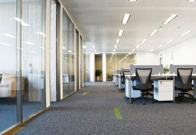 Modern hallway area featuring glass-walled offices and a glimpse of a lounge with a leather sofa.
