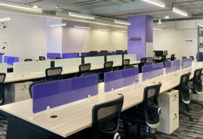 Spacious open-plan workspace featuring long rows of desks with purple privacy screens.