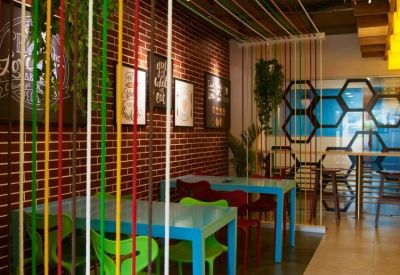 Colorful communal dining area with red brick walls, turquoise tables, and hanging rope partitions.