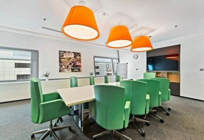 Vibrant meeting room with green chairs, a white conference table, and large orange lampshades.