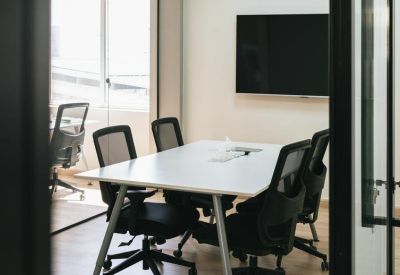Professional meeting room with a white table, mesh chairs, and wall-mounted screen.