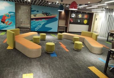 Modern lounge area featuring orange modular seating and yellow ottoman stools against a sport-themed mural.