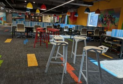 Co-working space with tall white bar stools and colourful floor accents.