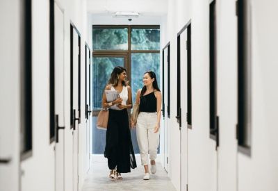 A bright white minimalist corridor with people walking past office doors.