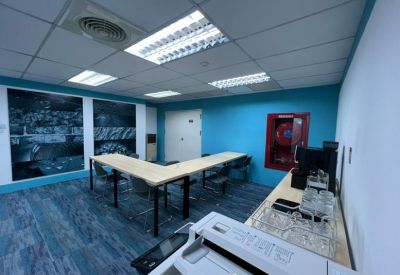 L-shaped wooden breakroom table in a communal area with blue walls and a printer.