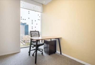 Private office with a light wood desk, ergonomic chair, and city views through a large window.