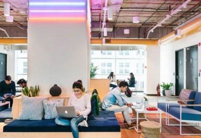 Modern coworking space with a central column, blue velvet sofas, and individuals working on laptops.