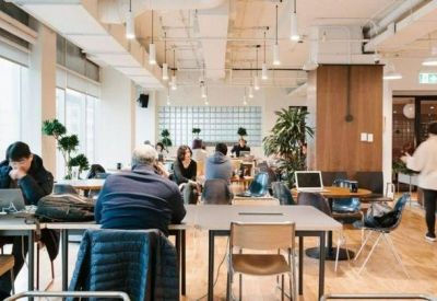 Coworking area with people working at long wooden tables under pendant lighting.