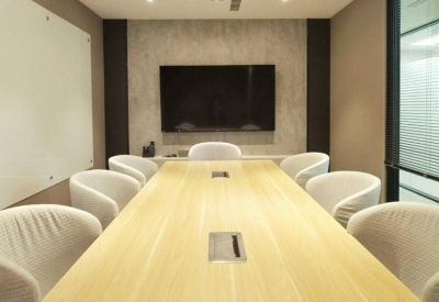 Bright boardroom with a large light wood table and wall-mounted screen.
