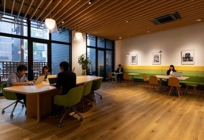 Coworking lounge with wood floors, green chairs, and large windows overlooking the street.