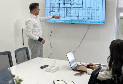 Meeting room with a large screen displaying architectural floor plans and a white conference table.
