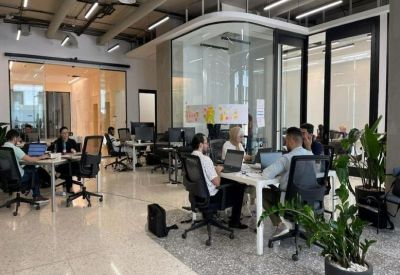 Spacious open-plan coworking area with glass-walled meeting pods and indoor plants.