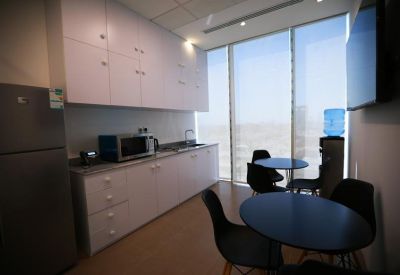 Office kitchen and break area with a fridge, microwave, and small round dining tables with chairs.