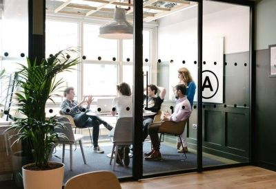 Glass-walled meeting room with a group of people seated around a table for a collaborative session.