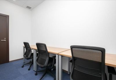 Narrow two-person office with simple wooden desks and black mesh chairs.