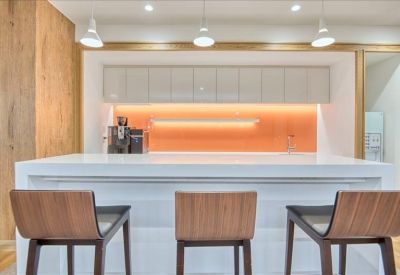 Sleek kitchen breakout area with a white island, wooden bar stools, and warm orange backsplash.