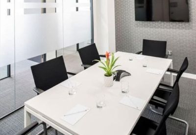 Professional meeting room with a white conference table, potted plant, and wall-mounted screen.