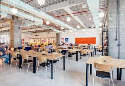 Large open-plan coworking space with wooden desks, ergonomic chairs, and industrial ceiling details.