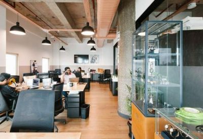 Open-plan office space with wooden desks, ergonomic chairs, and industrial ceiling details.