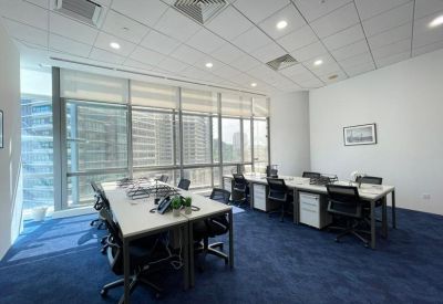 Spacious open-plan office with multiple desks and city views through large windows.