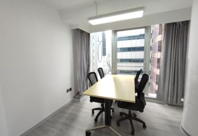 Bright private office featuring a wooden desk, mesh chairs, and large windows with urban views.