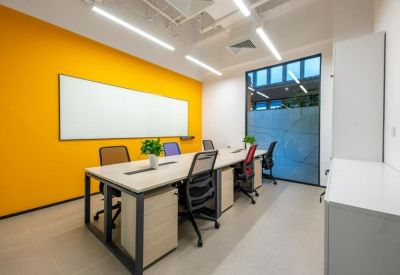 Bright office workspace with multiple desks, mesh chairs, and a bold yellow feature wall.