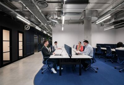 Spacious open-plan workspace with shared white desks and exposed industrial ceilings.