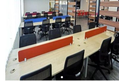 Bright open-plan office space with long wooden desks and orange privacy dividers.