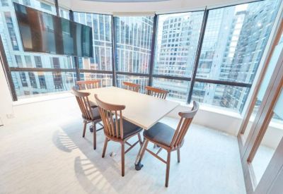 Sunlit meeting room featuring a wooden table and large windows overlooking high-rise city buildings.