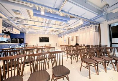 Versatile event space arranged with rows of wooden chairs and a presentation screen.