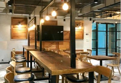 Long wooden coworking table under industrial pendant lighting and exposed ceiling.