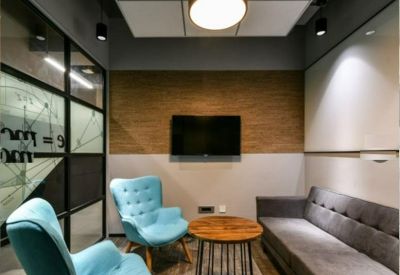 Modern lounge area with a grey sofa, teal wingback chairs, and a wooden accent wall.