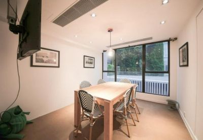 Bright meeting room with a large wooden table, patterned chairs, and a wall-mounted TV.