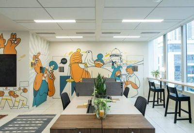 Creative workspace with a large colorful wall mural and tall black stools by the window.