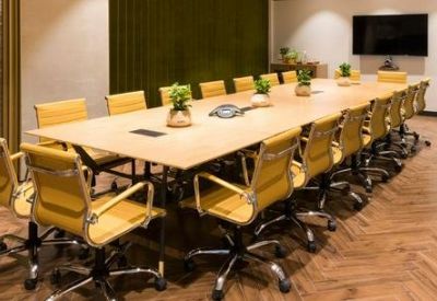 Large boardroom with a light wood table, yellow leather chairs, and green velvet curtains.