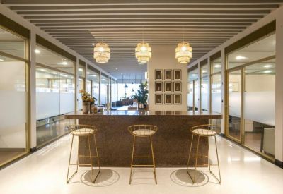 Modern stone-topped breakout bar with three golden stools and glass-walled office background.