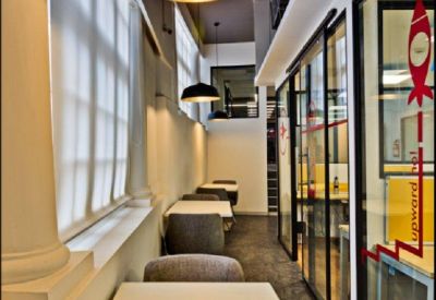 Narrow breakout area with small dining tables under a large gold-lined pendant lamp.