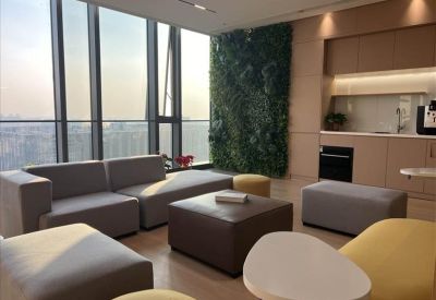 Bright communal lounge with a green living wall, modern grey sofas, and yellow ottomans.