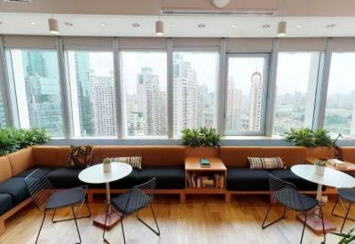 Communal lounge with orange and black banquette seating against large windows overlooking the city.